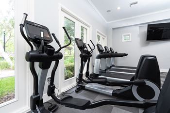 A room with a row of exercise machines in front of a window